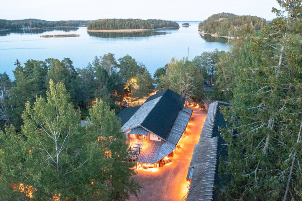 Herrankukkaro valaistuna pimenevänä iltana ilmasta kuvattuna, kauniin saaristomaiseman keskellä.