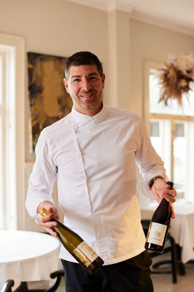 Ravintoloitsija Riccardo Soldati poseeraa hymyillen viinipullot käsissään.