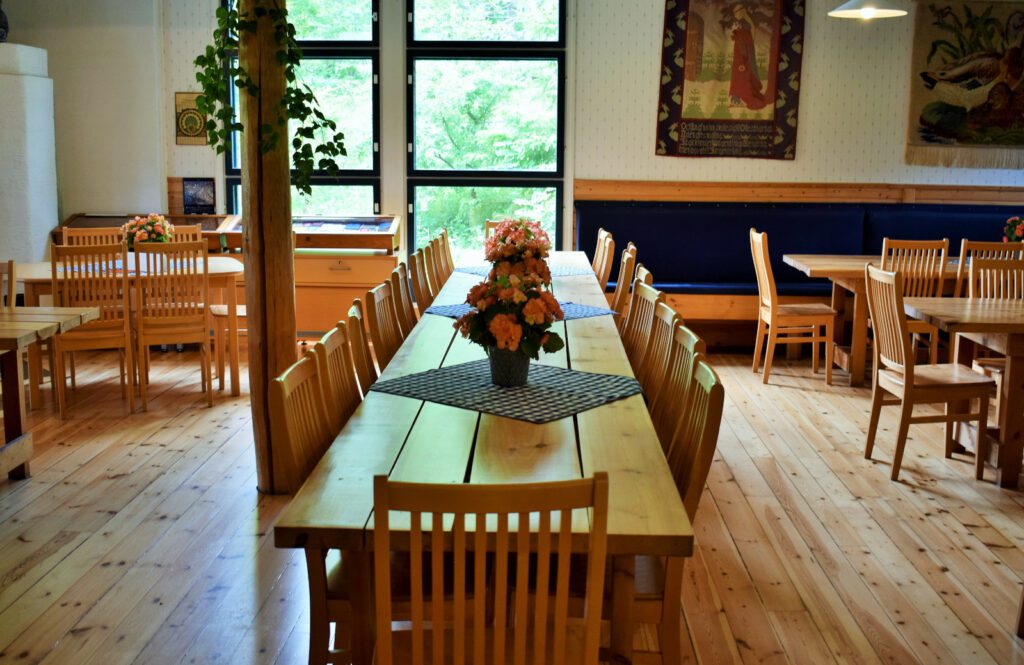Louhisaaren kartanon kahvilan sali, keskellä pitkä puinen pöytä ja useita tuoleja. Pöydän päällä sinivalkoisia ruutuliinoja ja niiden päällä oransseja kukkia ruukuissa.
