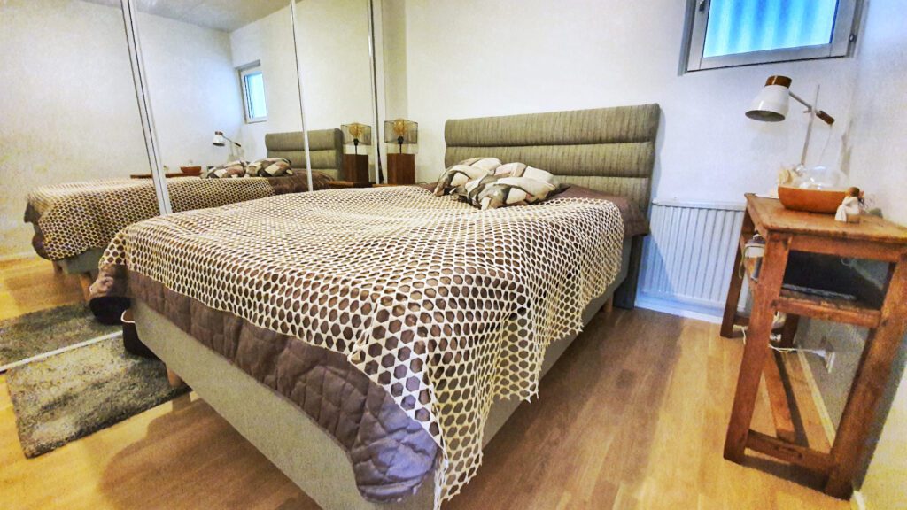 Huoneisto Merikorte makuuhuone, jossa parivuode harmaavalkoisella päiväpeitolla.