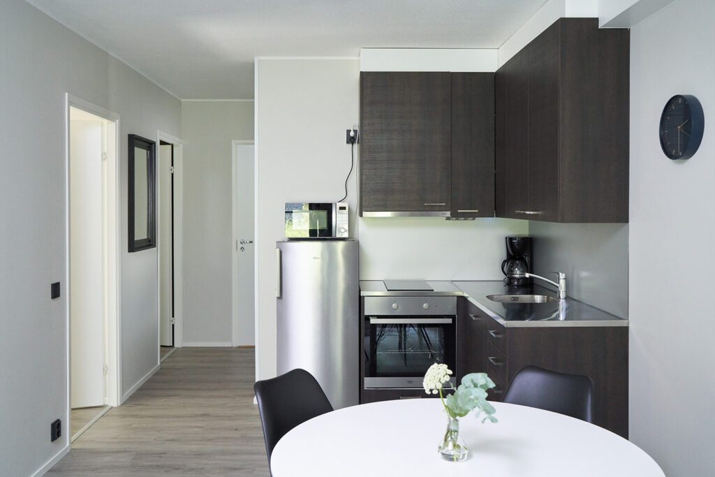 Naantali City Apartmentsin keittiö, jossa näkyy tummat keittiön kapit, uuni, harmaa jääkaappi ja pyöreä valkoinen pöytä.