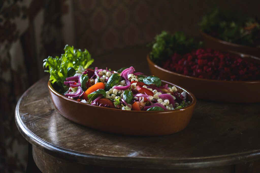 Ravintola Pohjakulman tarjoilupöydän salaattikulho, jossa punasipulia, mozzarellapalloja, tomaattia ja basilikaa.