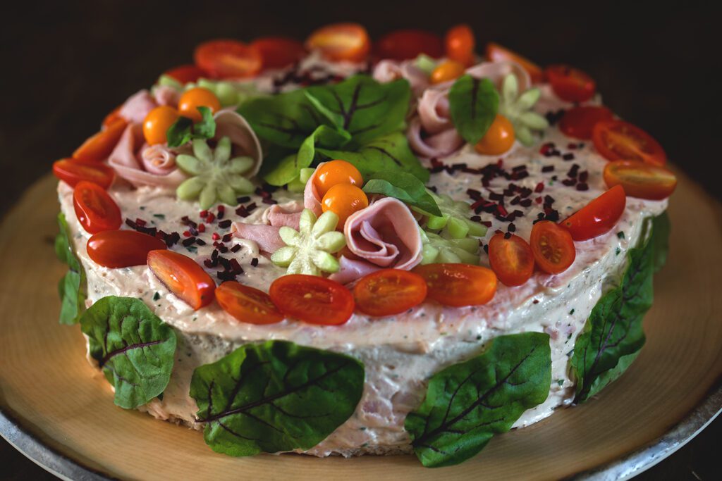 Ravintola Pohjakulman pyöreä voileipäkakku, joka on koristeltu kirsikkatomaatteja, kurkkua, kinkkua ja salaatinlehtiä.