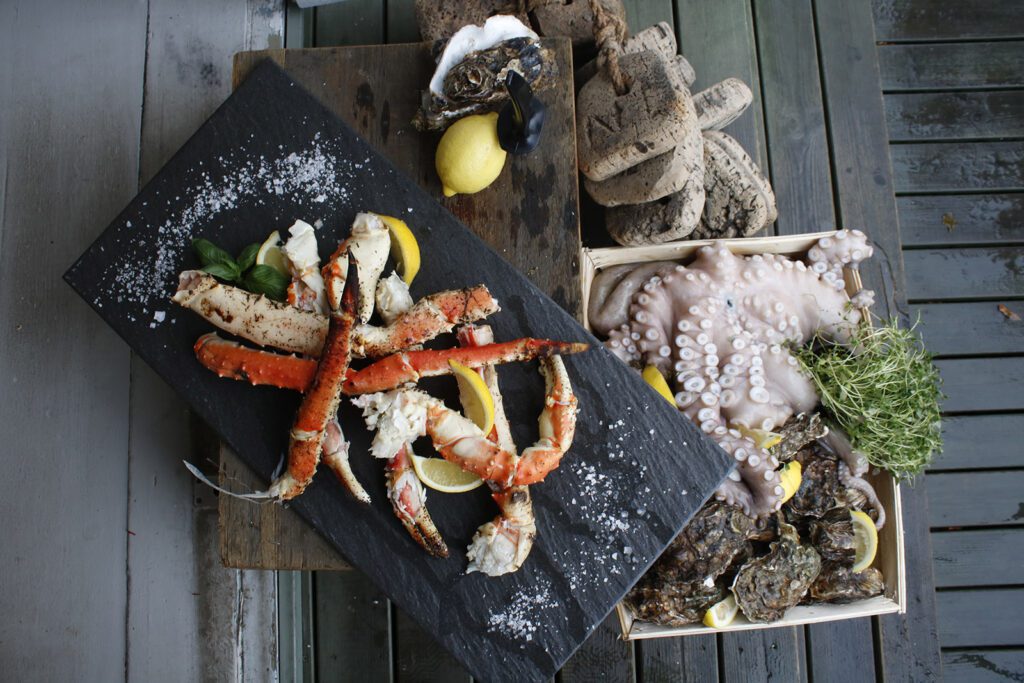 Snickari-ravintolan annoskuva, jossa tarjoiluastioiden päällä mereneläviä kuten mustekalaa, hummerin jalkoja ja simpukoita.