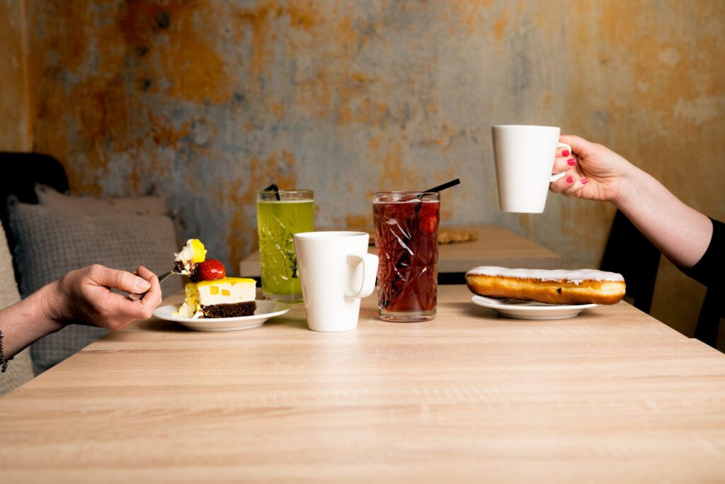 Naantalin Aurinkoisen kahvilan pöytä, jossa kaksi henkilöä nauttivat leivonnaisia, kahvia ja virvoitusjuomia.