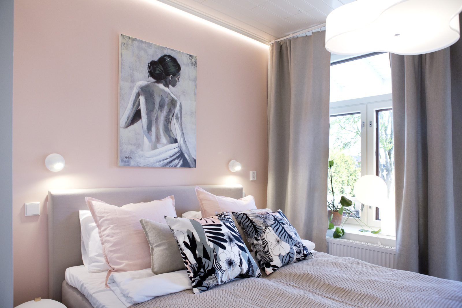 Hotelli Amandiksen huone, jossa vaaleanpunaiset seinät, taulu ja sänky, jossa mustavalkoisia koristetyynyjä.