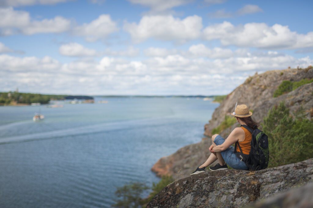 Nainen istuu Kuparivuoren kallioilla kesäpäivänä ja katselee alas merelle.