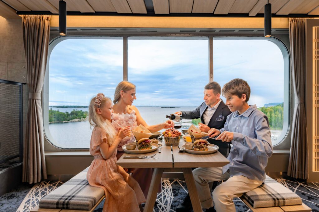 Perhe ruokailemassa Finnlinesin Fishermans Bistro -ravintolassa kaunis merinäkymä taustanaan.