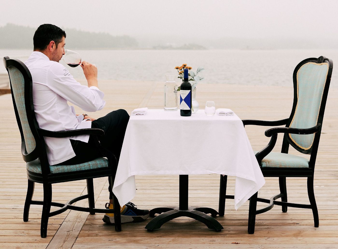 Tavastin Kilta -ravintolan ravintoloitsija istuu valkoinen kokinasu yllään ruokapöydän äärellä, maistaa viiniä ja katselee merelle.