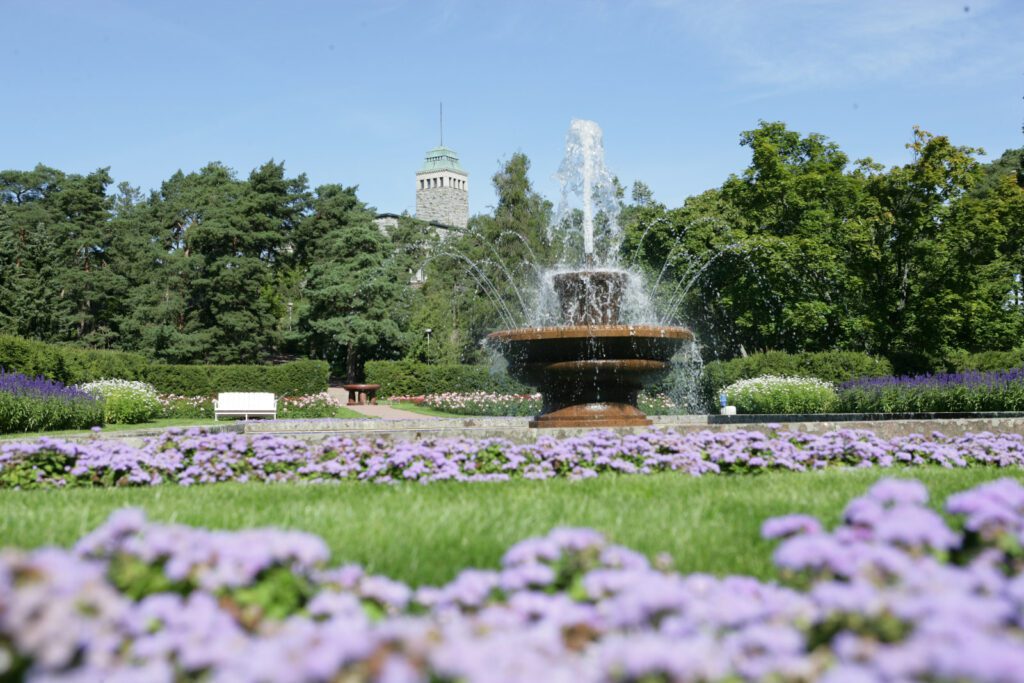 Kultrannan puutarhan iso suihkulähde, violetteja kukkia ja Kultarannan kivilinna.