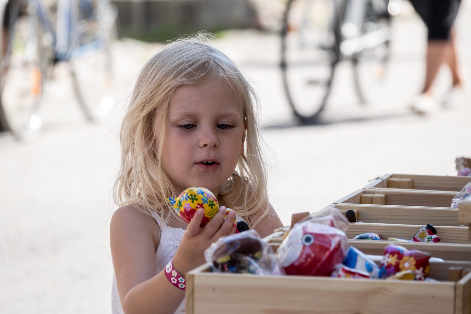 Vaaleahiuksinen tyttö pitää käsissään lelua, jonka on löytänyt myyntikojun laatikosta.
