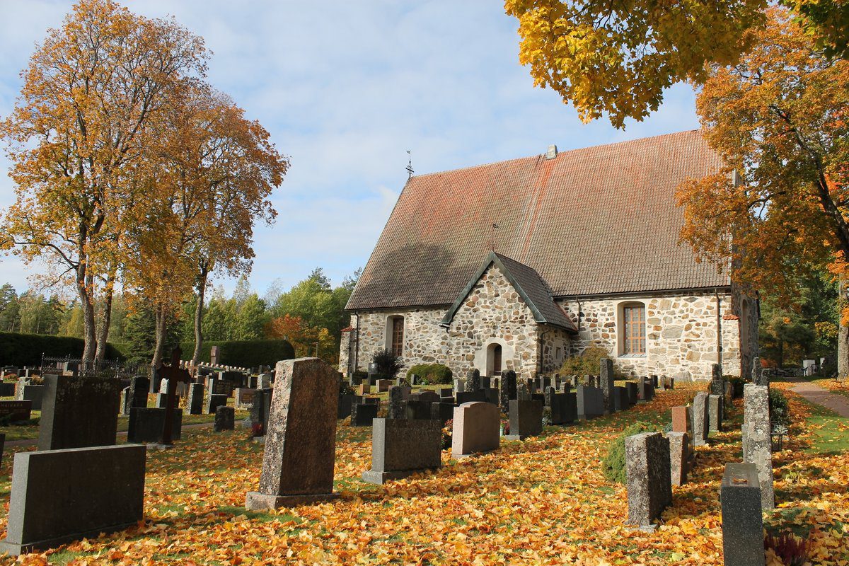 Lemun kirkko ja hautausmaa syksyllä, maassa ja puissa keltaisia lehtiä.
