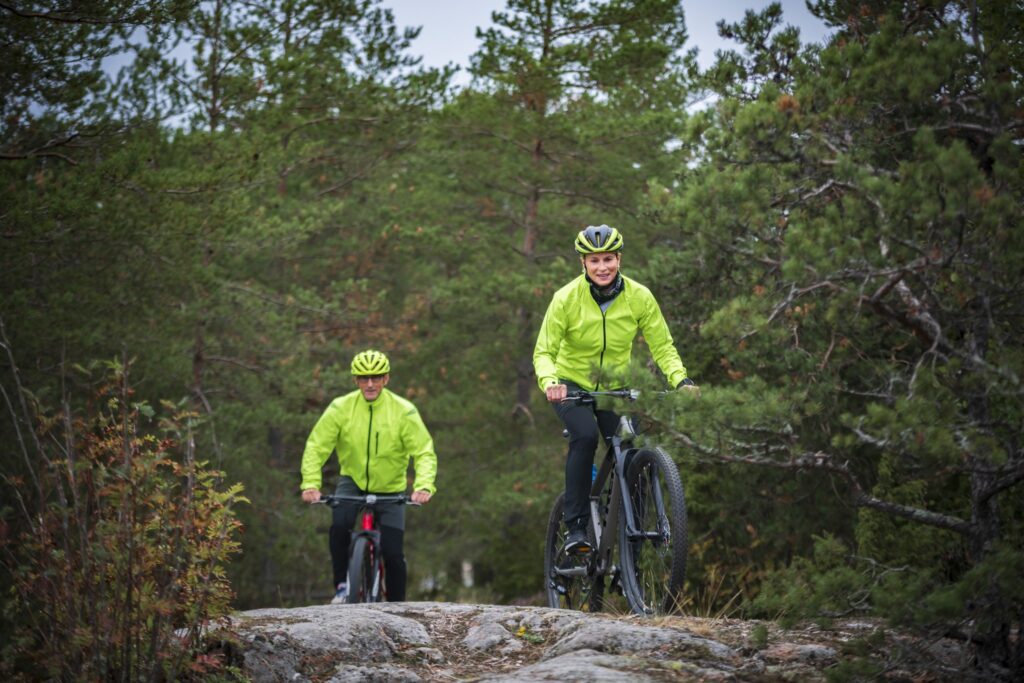 Nainen ja mies maastopyöräilevät kallioisella maastolla metsässä.