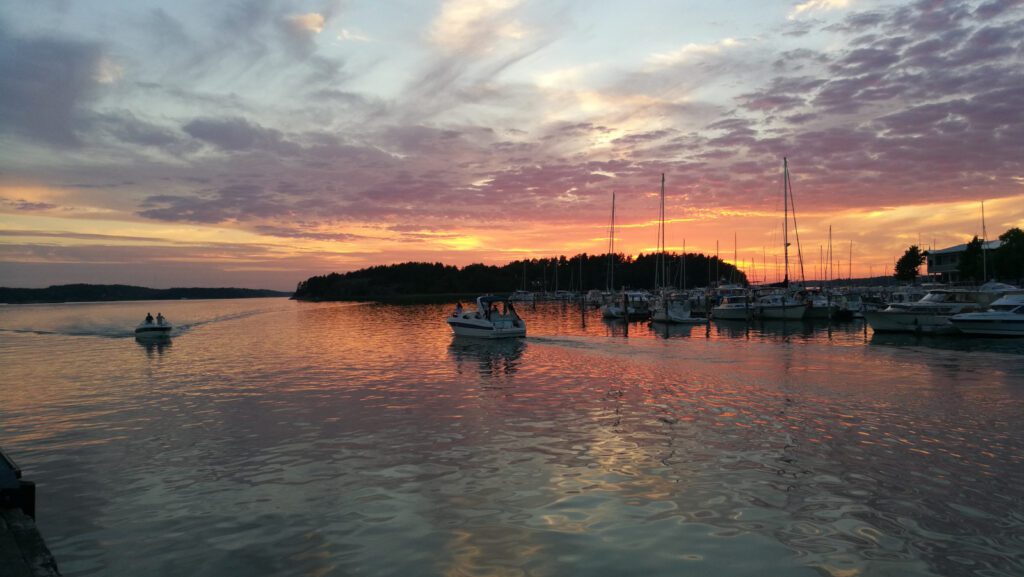 Auringonlasku Naantalin Vanhankaupungin rannassa ja veneilijöitä merellä.