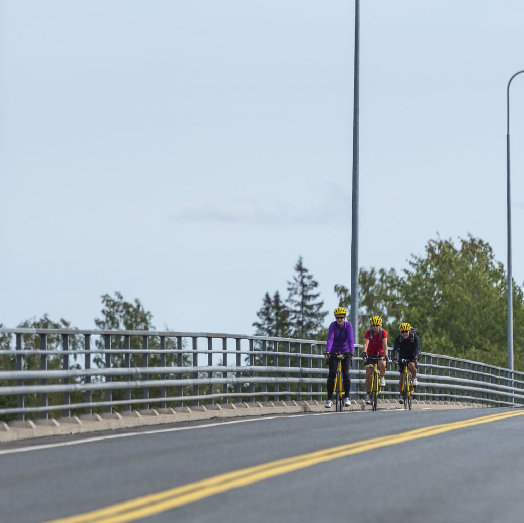 Kolme pyöräilijää pyöräilemässä sillalla.
