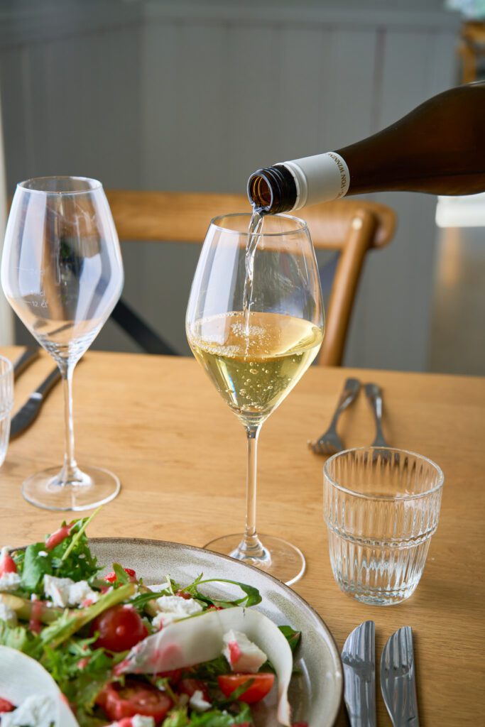 Pöydällä annos ja viinilaseja, joista yhteen tarjoilija kaataa viiniä.