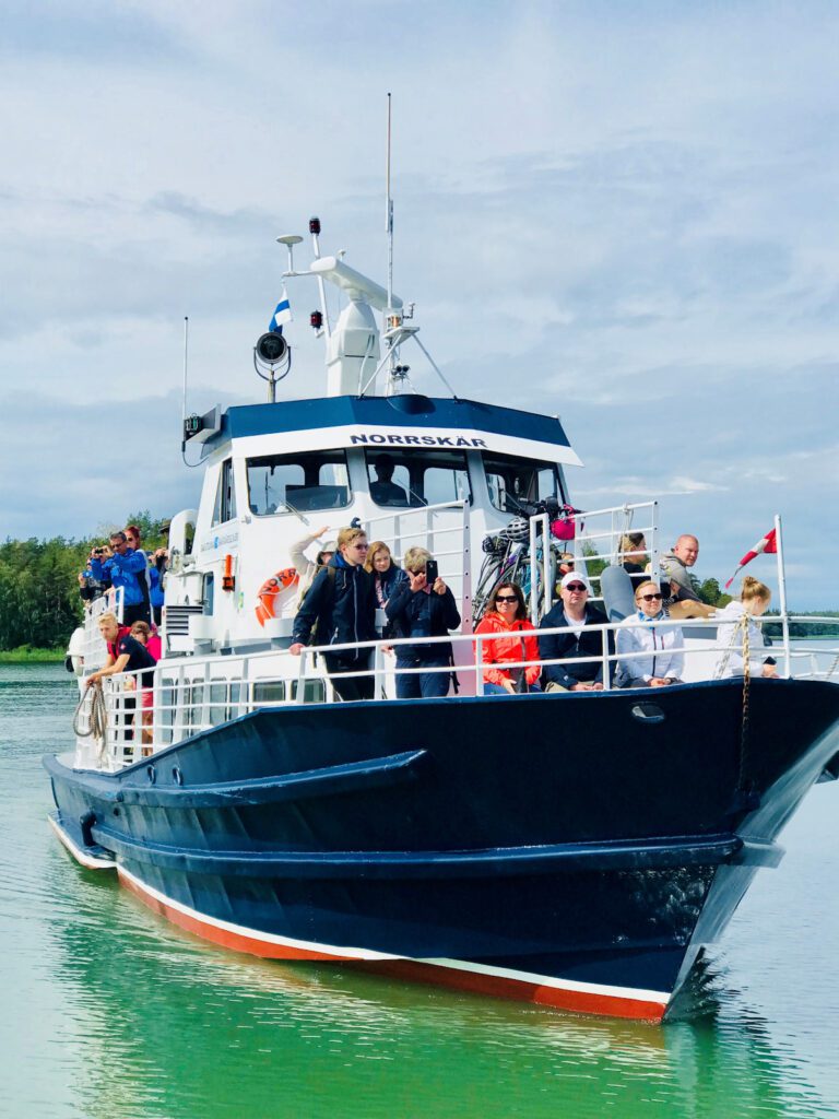 M/s Norrskär laivan edestä kuvattuna, ihmisiä kannella katsomassa saariston maisemia.