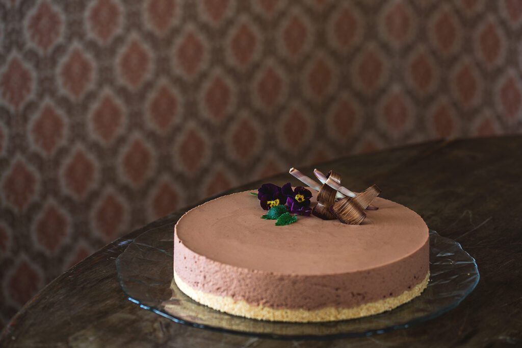 Ravintolassa valmistettu suklaajuustokakku, joka sointuu sävyiltään rusehtavaan kuviolliseen tapettiin.